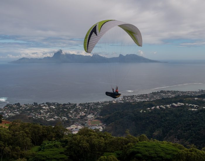A paraglider gracefully flies over rocky mountain peaks on a sunny day, offering a sense of adventure and freedom.